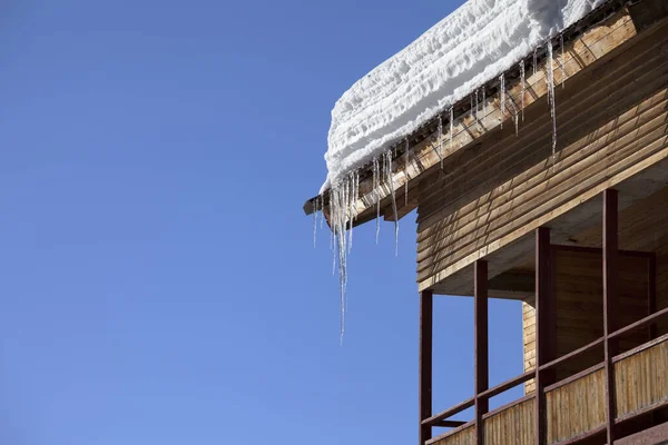 バルコニー付きの木造住宅で雪のコーニスとつららと屋根と太陽の下で澄んだ青空冬の日 — ストック写真