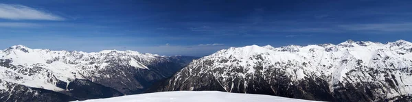 Panorama of high snow-capped mountain peaks and beautiful sky with clouds at sunny day. Caucasus Mountains in winter, region Dombay.