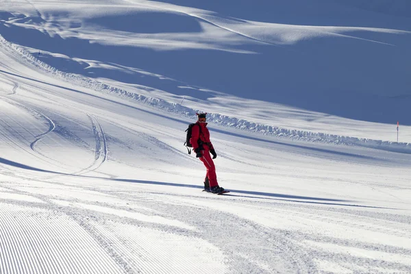 日当たりの良い冬の夜にグルーミングマシンで準備された雪の日差しのあるスキー場の赤い下り坂のスノーボーダー — ストック写真