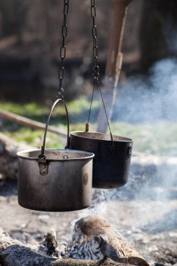 Güneşli yaz gününde ormanda dumanla yanan iki eski kazan.
