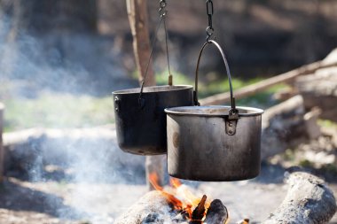Güneşli yaz gününde, ormanda dumanla şenlik ateşinde iki eski kazanda yemek pişirmek.
