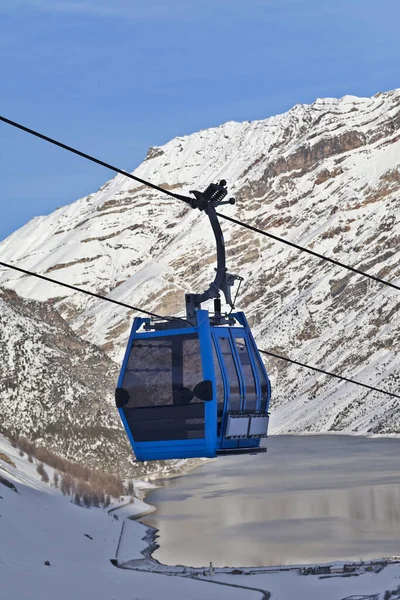 Blue gondola lift, snowy off-piste ski slope in high winter mountains, village and big lake at background. Italian Alps at evening. Livigno, region of Lombardy, Italy, Europe.