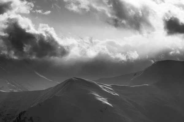 Snowy evening mountain and sunlight clouds. View from ski slopes at winter. Caucasus Mountains, Georgia, region Gudauri. Black and white toned landscape.
