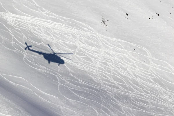 Shadow from helicopter on snowy off-piste ski slope with traces from skis and snowboards at sunny winter day. Heli-ski in high mountains.