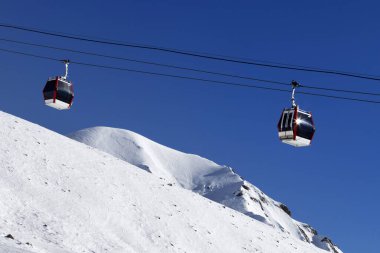 Gondola lift, snowy off-piste ski slope, high winter mountains and blue clear sky in sunny day. Caucasus Mountains. Georgia, region Gudauri.