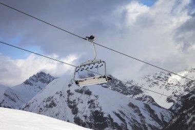 Sunlit chair lift, snowy ski slope, high winter mountains and blue cloudy sky. Ski area Mottolino Fun Mountain, Italian Alps. Livigno, Lombardy, Italy, Europe.