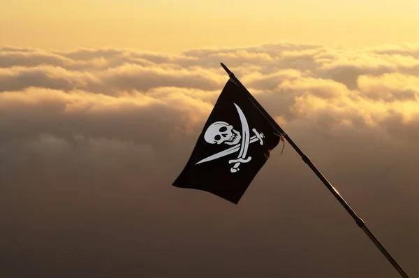Jolly Roger (pirate flag) on wind and sea in sunset cloudy sky at background