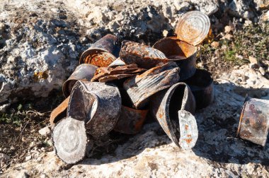 Group of old rusty tin cans covered with ash on stones at sunny day. Concept of environmental pollution, ecological problems.