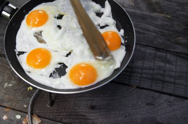 Fried eggs cooked in frying pan on camping gas stove on old wooden table. Outdoor cooking.