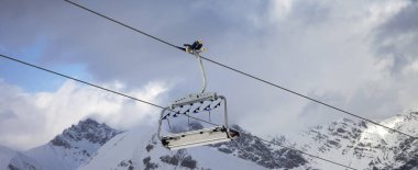 Sunlit chair lift, snowy ski slope, high winter mountains and blue cloudy sky. Ski area Mottolino Fun Mountain, Italian Alps. Livigno, Lombardy, Italy, Europe. Panoramic view.