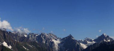 Panorama of high rocky mountains with snow and glacier, sunlit blue sky with clouds at summer morning. Caucasus Mountains. Georgia, region Svanetia.
