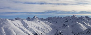 Panorama of snowy slope in high winter mountains and sunlit cloudy sky at evening. Italian Alps. Livigno, region of Lombardy, Italy, Europe.