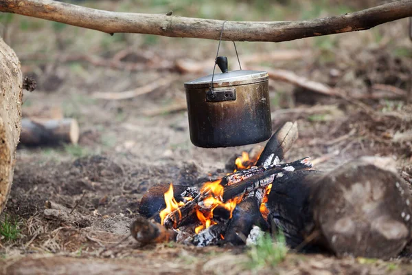 Outdoor cooking in old sooty cauldron on campfire at forest