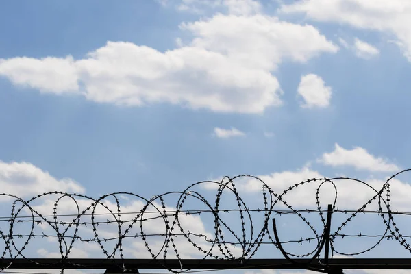 Black coiled barbed wire fence and blue sky with sunlit clouds at background