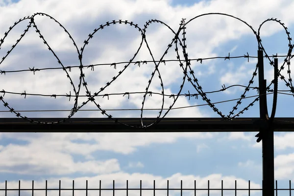 Black coiled barbed wire fence and blue sky with sunlit clouds at background in evening