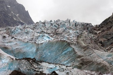 Glacier with deep crevasses covered with snow and ground in high rocky mountains at gray day. Caucasus Mountains. Georgia, region Svanetia.