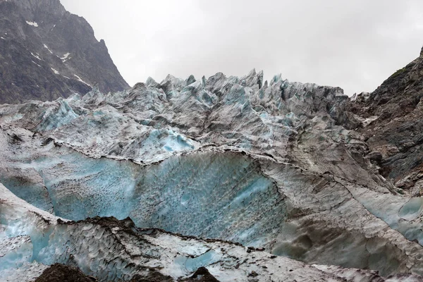 Glacier with deep crevasses covered with snow and ground in high rocky mountains at gray day. Caucasus Mountains. Georgia, region Svanetia.