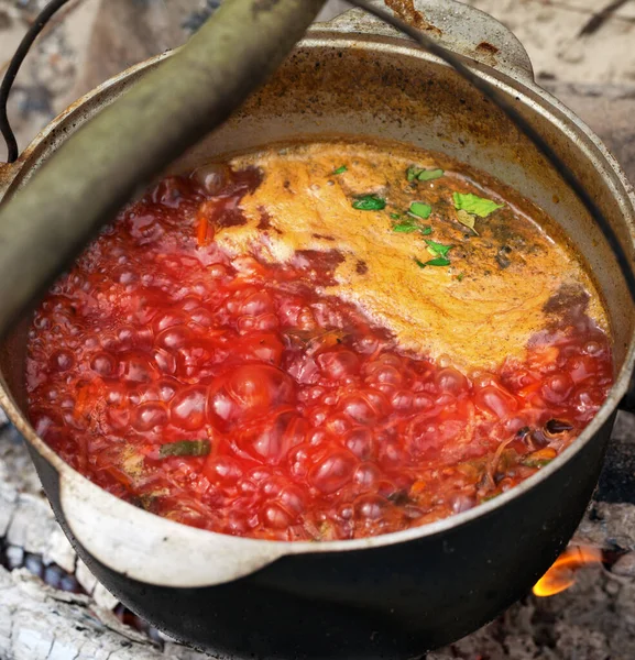 Borscht - Ukrainian traditional soup cooking in old sooty cauldron on campfire at summer day. Close-up view