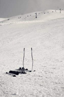Skiing equipment: ski poles, skis on snowy slope, chair lift and gray cloudy sky at background. Ski area Mottolino, Italian Alps in winter. Livigno, Lombardy, Italy Europe. Black and white retro toned.