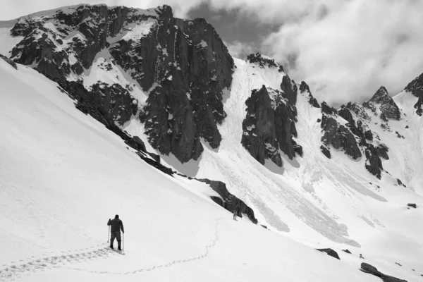 Snowy mountains with avalanche traces, sunlit cloudy sky, hiker with ski poles and dog on snowy slope at sunny day. Turkey, Kachkar Mountains, Pontic Mountains. Black and white toned landscape.