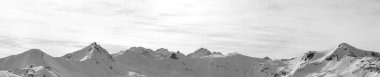 Panorama of high winter mountains with snowy slopes and sunlight cloudy sky at morning. Italian Alps. Livigno, region of Lombardy, Italy, Europe. Black and white toned landscape.