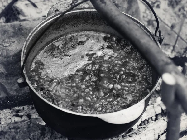 Borscht - Ukrainian traditional soup cooking in old sooty cauldron on campfire at summer day. Black and white toned image.