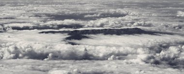 Panoramic aerial view on clouds and mountains in sun day. Black and white toned landscape.