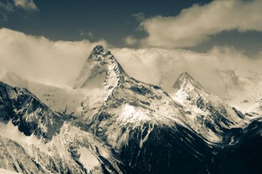 High winter snowy mountains in clouds. Caucasus Mountains, region Dombay, Mount Belalakaya. Retro color toned landscape.