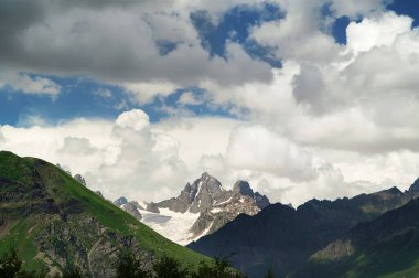 High rocky mountains with snow and glacier, sunlit blue sky with clouds at summer evening. Caucasus Mountains. Georgia, region Svanetia.