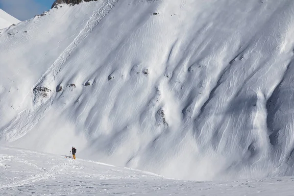 Skiers and off-piste slope with traces of skis, snowboards and avalanches. Caucasus Mountains in sunny winter day, Georgia, region Gudauri.