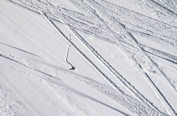 Groomed snowy ski slope with trace from skis, snowboards and stone at sun winter day