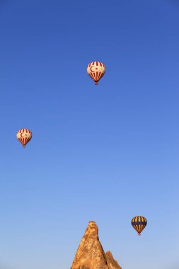 GOREME, CAPPADOCIA, TURKEY - MAYIS, 2013: Güneşli sabahın erken saatlerinde açık mavi güneşli gökyüzü ve kaya oluşumları üzerine Türk sembolik sıcak hava balonları