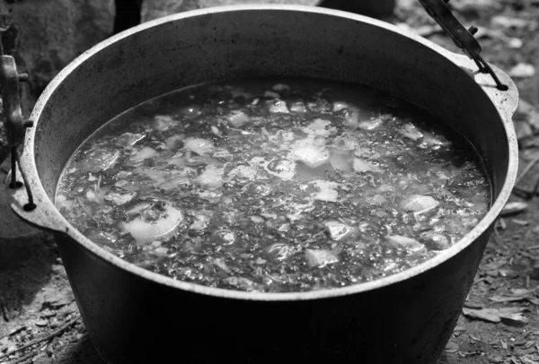 Freshly cooked hot soup in sooty cauldron on camp fire. Outdoor camping cooking. Black and white toned image