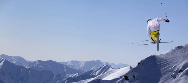 在阳光明媚的冬日 自由式滑雪带着交叉滑雪板在多雪的山上跳跃 全景视图 — 图库照片
