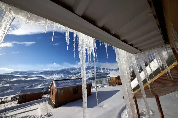 雪の多い冬の山で大きな日光のつららや小さな木造住宅と屋根 コーカサス山脈 シャハーグ アゼルバイジャン 広角ビュー — ストック写真