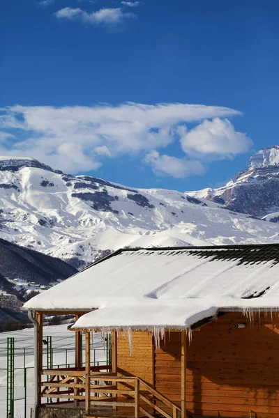 Holzhaus Mit Schneebedecktem Dach Und Eiszapfen Schneebedeckten Winterbergen Und Blauem — Stockfoto
