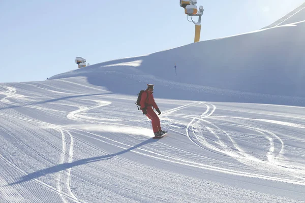 日当たりの良い冬の日にグルーミングマシンで準備された雪の斜面に赤のスノーボーダーが降ります — ストック写真