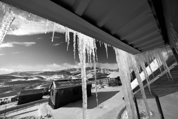 Dach Mit Großen Sonnenbeschienenen Eiszapfen Und Kleinen Holzhäusern Verschneiten Winterbergen — Stockfoto