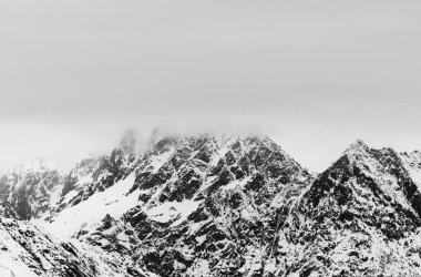 Karda kayalık dağlar ve kış günü bulutlu gri gökyüzü. Kafkasya Dağları, Gürcistan 'ın Svaneti bölgesi. Siyah ve beyaz tonlu manzara.