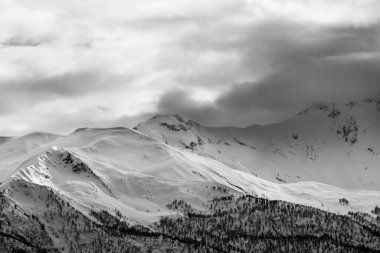 Akşam güneşli karlı dağlar ve gri bulutlu gökyüzü. Kışın Kafkas Dağları. Georgia, bölge Svanetia. Siyah ve beyaz tonlu manzara.