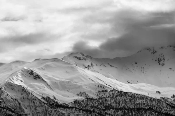 Akşam güneşli karlı dağlar ve gri bulutlu gökyüzü. Kışın Kafkas Dağları. Georgia, bölge Svanetia. Siyah ve beyaz tonlu manzara.