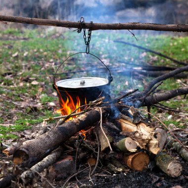 Sonbahar ormanlarında kamp ateşinde eski, ıslak bir kazanda yemek pişirmek. 