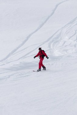Kar yağışı sonrası gri kış gününde kar yamaçlarında kırmızı tepedeki snowboardçu.