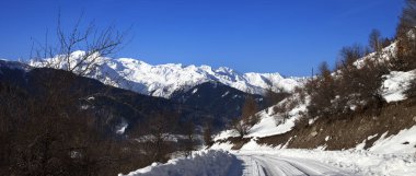 Kışın karlı dağlarda, güneşli ve soğuk bir sabahta buzla kaplı bir yol. Kafkas Dağları. Georgia, bölge Svaneti. Panoramik görünüm.