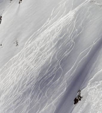 Güneşli kış akşamlarında kayak ve snowboard izleri olan karlı bir pistte kayak pisti.