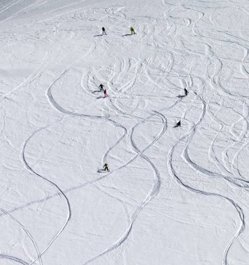 Snowboardcular ve kayakçılar yüksek kış dağlarındaki karlı yokuş aşağı inerler. Yukarıdan görüntüle.
