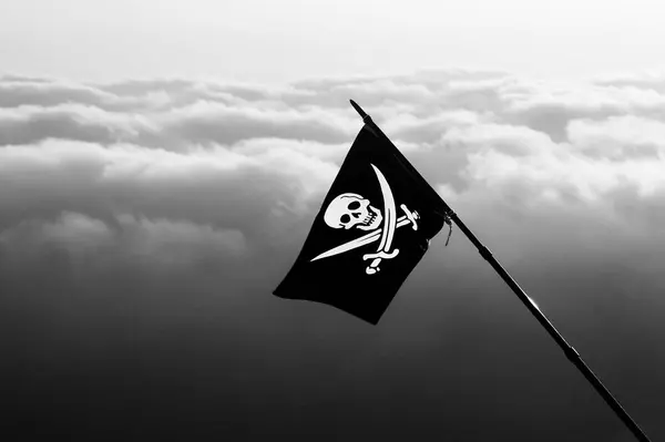 Jolly Roger - pirate flag on wind and sea in cloudy sky at background. Black and white toned image.