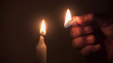 Erkek ellerinin bir mumu kibritle yakması, evin içinde alevlerin sürekli yanması.