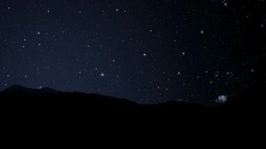 Gece gökyüzünde dağların manzarasıyla yıldızların hareketi