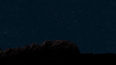 Gece gökyüzünde dağların manzarasıyla yıldızların hareketi